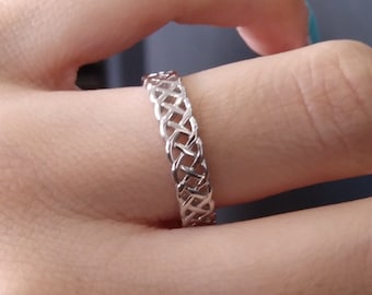 Pode incluir: Um anel de prata com um design trançado. O anel é usado em um dedo.