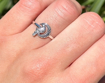 May include: A silver ring with a bird perched on a crescent moon design.