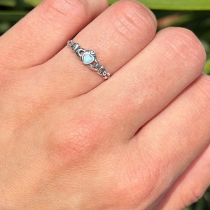 May include: A silver ring featuring a heart-shaped opal stone set within a Celtic knot design.