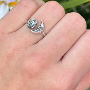 May include: A silver ring with a sun and moon design. The sun is on the left side of the ring and the moon is on the right side. The ring is adjustable.