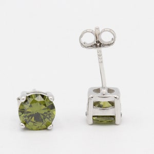 May include: A pair of silver stud earrings with a round, green gemstone in each. The earrings have a post and butterfly back.