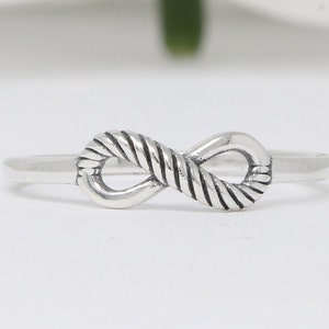 May include: A silver infinity ring with a rope-like design. The ring is simple and elegant.