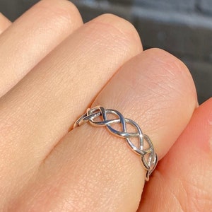 Könnte beinhalten: Ein silberner geflochtener Ring an einem Finger mit leuchtend gelbem Nagellack.