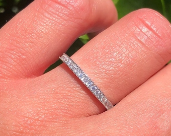 May include: A thin silver band with a row of small, clear gemstones set in a pave setting.
