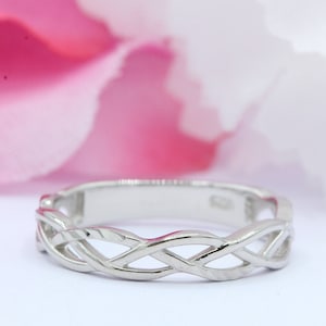 May include: A silver Celtic knot ring with a braided design. The ring is on a white background.