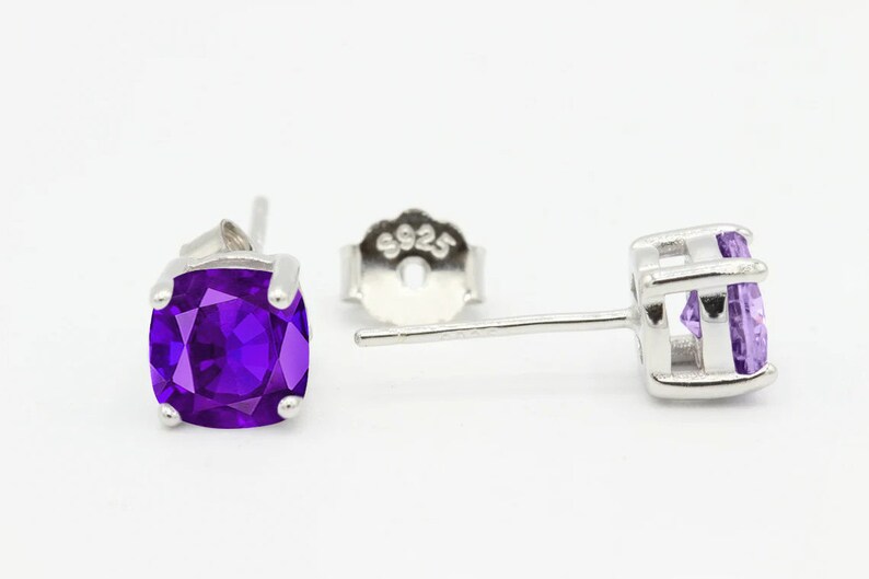 May include: A pair of silver stud earrings with a square purple amethyst gemstone. The earrings have a post and butterfly back.