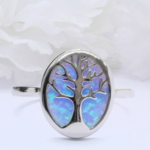 May include: A silver ring with a blue opal tree of life design. The ring is oval shaped and has a smooth, polished finish.
