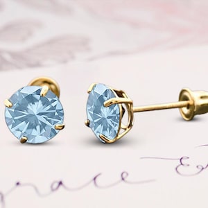 May include: A pair of gold stud earrings with light blue round gemstones. The earrings have a screw-back closure.