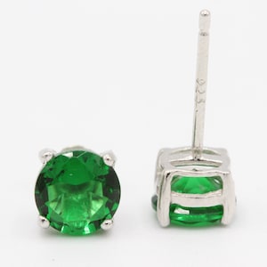 May include: A pair of silver stud earrings with a round green gemstone in each earring.