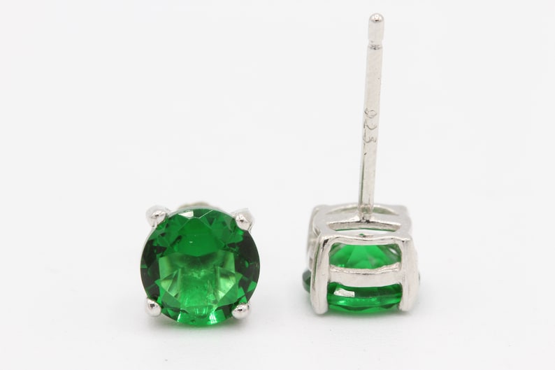 May include: A pair of silver stud earrings with a round green gemstone in each earring.