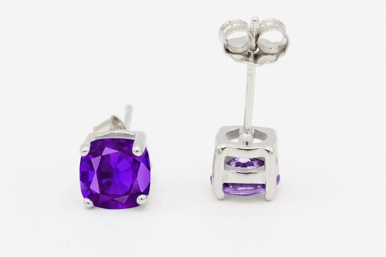 May include: A pair of silver stud earrings with a square-shaped amethyst gemstone in the center. The earrings have a post and butterfly back.