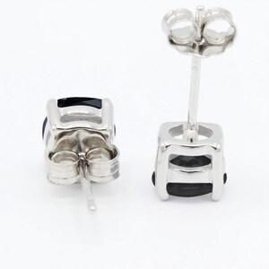 May include: A pair of silver stud earrings with black gemstones. The earrings have a square shape and a simple design.