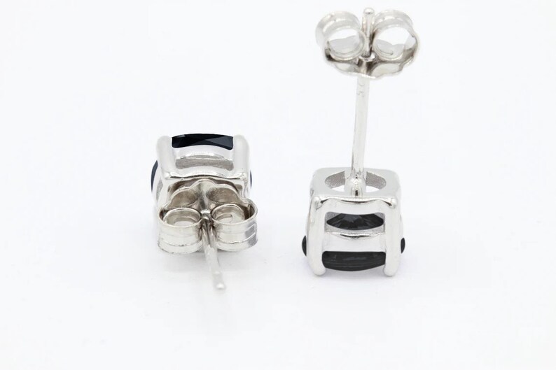 May include: A pair of silver stud earrings with black gemstones. The earrings have a square shape and a simple design.