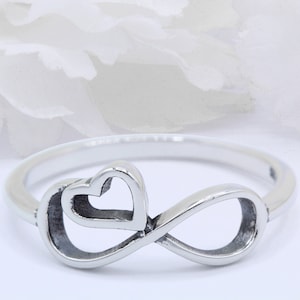 May include: A silver ring featuring an infinity symbol with a heart design. The heart is interwoven with the infinity symbol.