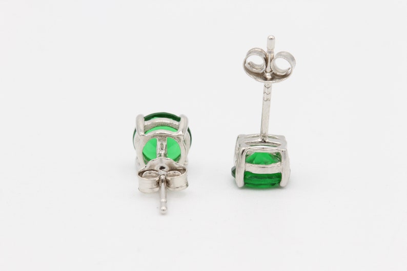 May include: A pair of silver stud earrings with green gemstones. The earrings have a simple design and are perfect for everyday wear.