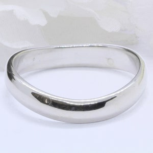 May include: A simple, smooth, silver wedding band with a rounded, slightly curved shape.