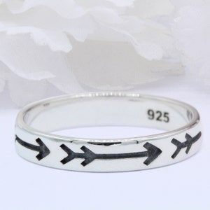 May include: A silver ring with four black arrow designs around the band. The ring is stamped with the number "925" on the inside.