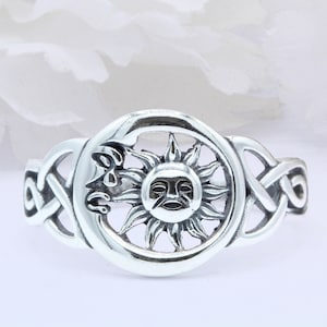 May include: A silver ring with a Celtic knot design and a sun with a face in the center.