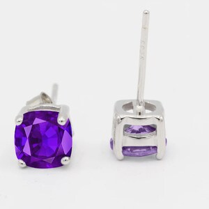 May include: A pair of silver stud earrings with a square purple gemstone.