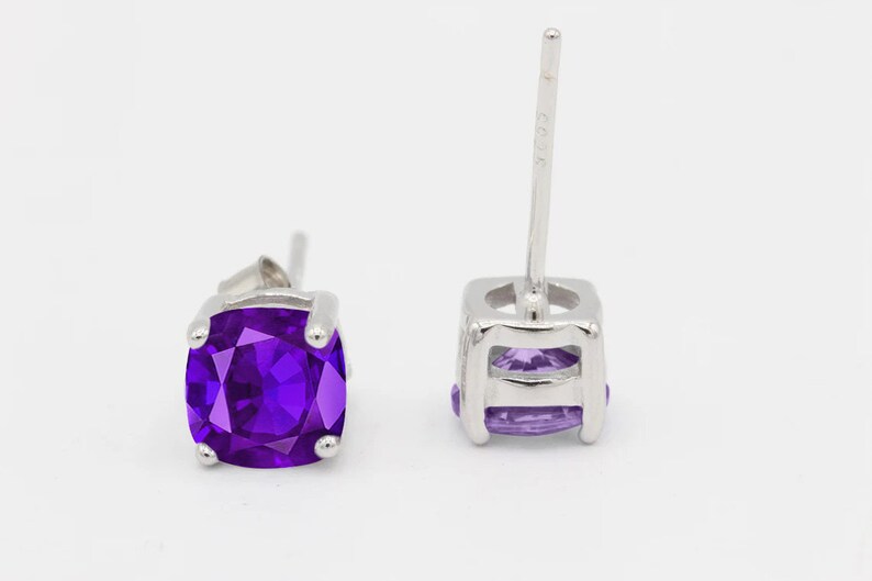 May include: A pair of silver stud earrings with a square purple gemstone.