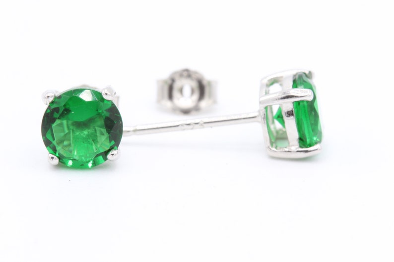 May include: A pair of silver stud earrings with green gemstones.