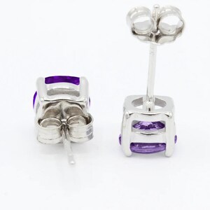 May include: A pair of silver stud earrings with a purple gemstone in each. The earrings have a simple, elegant design.