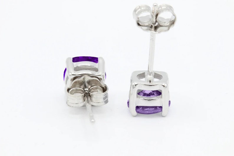 May include: A pair of silver stud earrings with a purple gemstone in each. The earrings have a simple, elegant design.