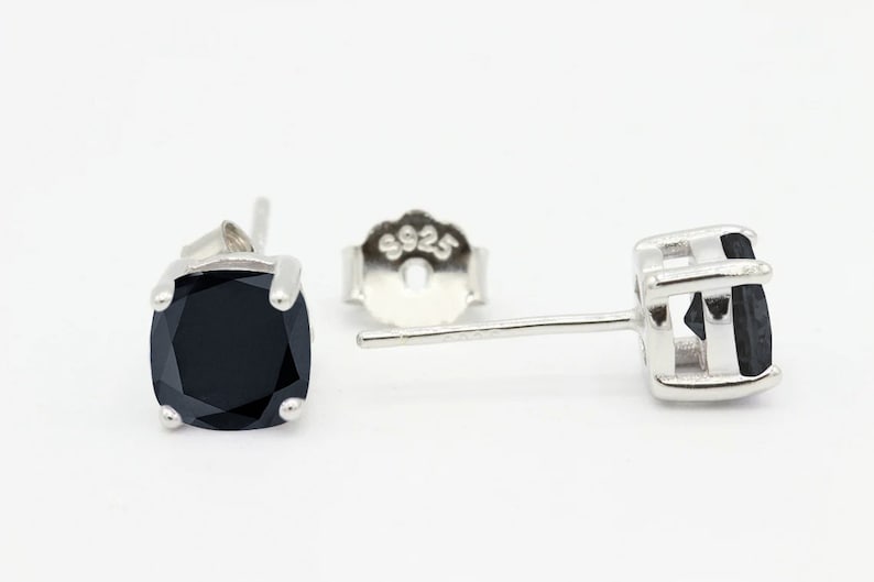 May include: A pair of silver stud earrings with black square-shaped gemstones. The earrings have a post and butterfly back.
