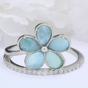 May include: A silver ring with a blue and green flower design. The flower is made of a gemstone and is surrounded by a band of small clear stones.