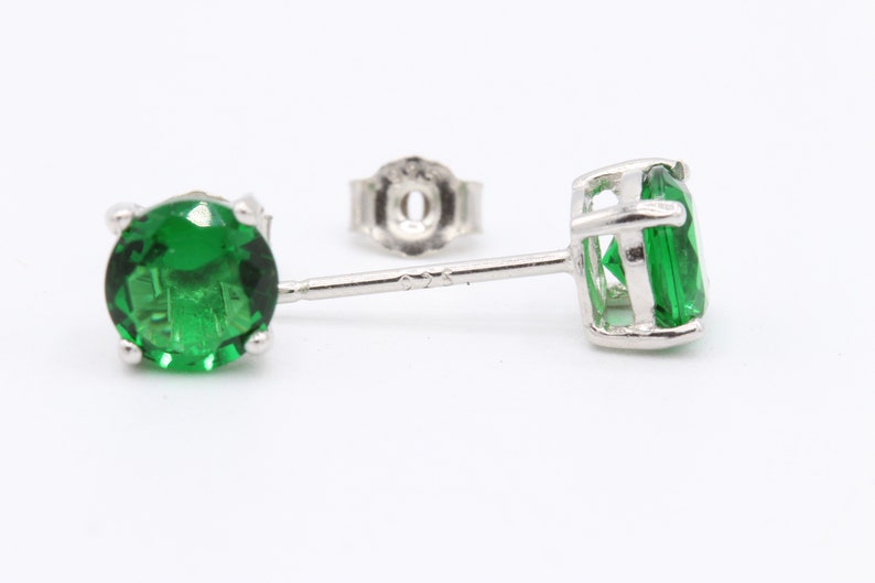 May include: A pair of silver stud earrings with green gemstones. The earrings have a post back fastening.