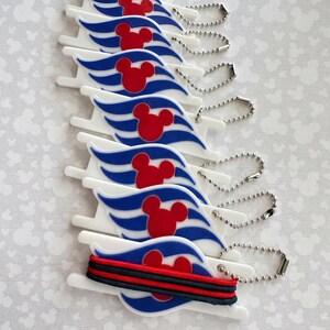May include: A stack of white plastic tags, each featuring a blue wave design and a red Mickey Mouse head silhouette. Each tag includes a silver metal ball chain attached to the top corner. The bottom tag is wrapped with a black and red elastic band.