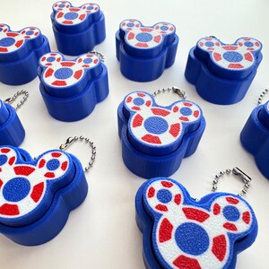 May include: A collection of ten blue plastic keychains shaped like a three-circle head silhouette. Each keychain features a white top surface with a red and blue patterned design and a silver-toned metal ball chain attached to the top.