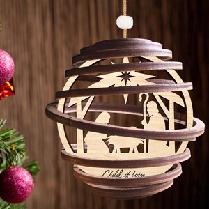 Puede incluir: Un adorno navide&ntilde;o de madera con un dise&ntilde;o en capas que representa la escena de la natividad. El adorno es marr&oacute;n y presenta una estrella, un pesebre y el texto "Child is born".