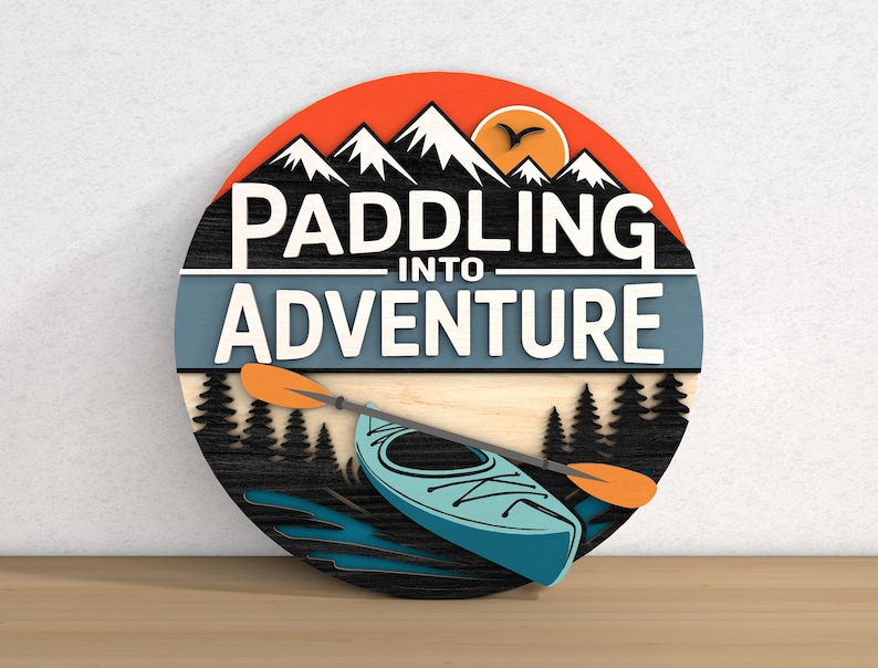 May include: A round wooden sign with the words "Paddling Into Adventure" in white. The sign features a mountain range, a kayak, and a paddle. The color scheme includes orange, blue, black, and white.