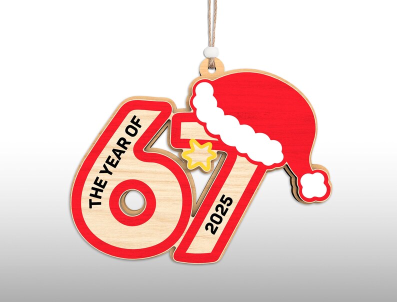 May include: Wooden Christmas ornament with the text "THE YEAR OF 67 2025" in red and black. The ornament features a red Santa hat and a yellow star. The ornament is hanging by a string.