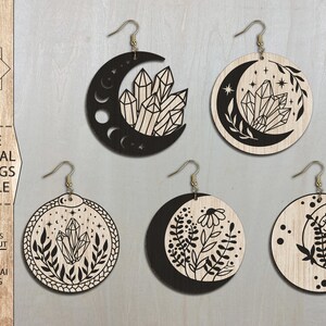 May include: Set of six laser cut earrings featuring crescent moons with various designs. The designs include crystals, flowers, and leaves. The earrings are made of wood and are black in color.