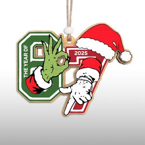 May include: Wooden Christmas ornament with the numbers 9 and 7, and the year 2025. The number 9 features a green hand with a red and white cuff, making an "okay" gesture. The number 7 has a Santa hat and a white hand pointing down.