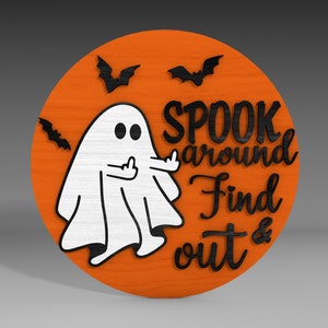 Op de afbeelding: Een rond, oranje houten bord met een witte geest die de middelvinger opsteekt. Het bord zegt "Spook around Find out &" in zwarte letters. Er zijn drie zwarte vleermuizen op het bord.