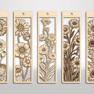 May include: Five wooden bookmarks with floral designs. Each bookmark features a different laser-cut flower arrangement, including sunflowers and other blooms, set within a rectangular frame. The bookmarks have a small hole at the top for a tassel or string.