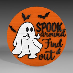 Op de afbeelding: Een rond, oranje houten bord met een witte geest die de middelvinger opsteekt. Het bord zegt "Spook around Find out &" in zwarte letters.