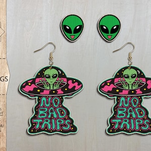 May include: A pair of wooden earrings featuring a cartoon alien in a UFO with the text "No Bad Trips". The earrings are pink, black, green, and blue.