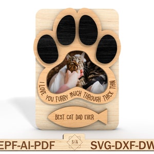 Puede incluir: Un marco de fotos de madera con forma de huella de pata con un recorte para una foto. El marco tiene el texto "I love you furry much through thick and thin" y "Best cat dad ever" con un icono de pez.