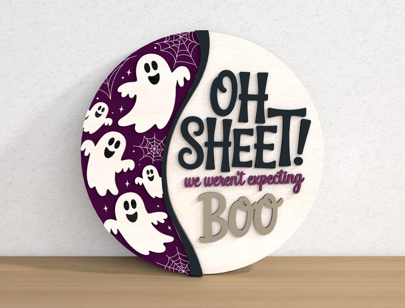 以下が含まれることがあります： ハロウィーンをテーマにした丸い木製の看板。看板は、黒で「OH SHEET!」、紫で「we weren't expecting」、グレーで「BOO」というテキストが書かれた白い背景が特徴です。白い幽霊とクモの巣が付いた紫色の三日月が左側にあります。