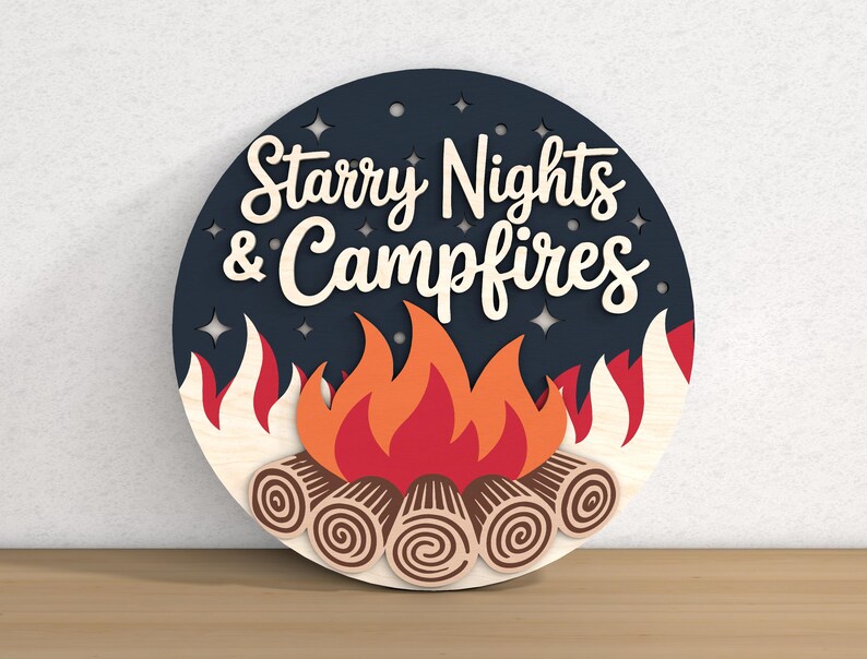 May include: A round wooden sign with the words "Starry Nights & Campfires" in white script. The sign features a campfire design with flames in red, orange, and white, and logs at the base. The background is dark blue with star cutouts.