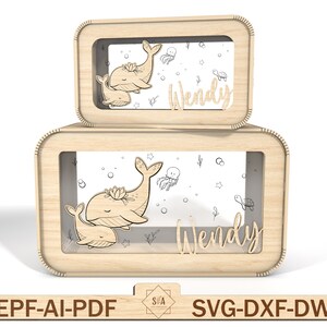 Puede incluir: Dos cajas de madera con un dise&ntilde;o de ballena y ballenato. Las cajas tienen una ventana transparente y el nombre "Wendy" est&aacute; escrito en la parte delantera.