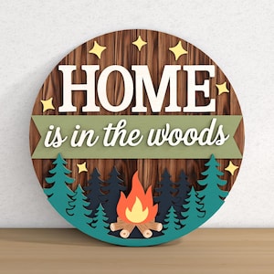 May include: A round wooden sign with the text "HOME is in the woods". The sign features a wood grain background, white lettering, and a forest scene with a campfire. Yellow star accents are also included.
