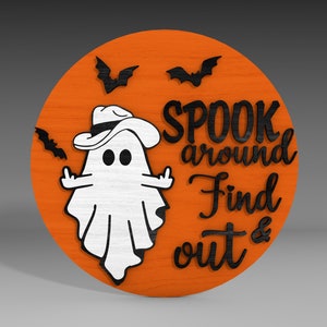 Op de afbeelding: Een rond, oranje houten bord met een witte geest die een zwarte cowboyhoed draagt en de tekst "SPOOK around Find out &" in zwart.