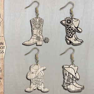 May include: Four pairs of laser cut western cowgirl boot earrings. Each pair features a boot with a cowboy hat on top. The boots are detailed with stitching and a spur. The earrings are made of wood and have a gold finish.