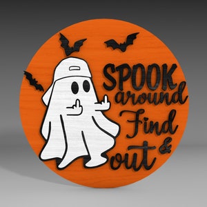 Op de afbeelding: Een rond, oranje houten bord met een zwarte geest die een baseballpet achterstevoren draagt en de middelvinger opsteekt. Het bord zegt "Spook around Find out &" in zwarte letters.