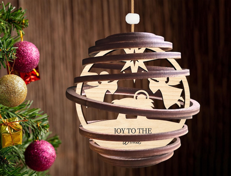 Puede incluir: Un adorno navide&ntilde;o de madera con un dise&ntilde;o en capas que representa una escena de la natividad. El adorno es marr&oacute;n y tiene la inscripci&oacute;n "Joy to the World".